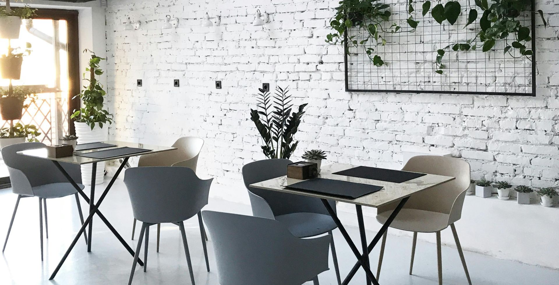 A chic, contemporary cafe interior featuring white brick walls, modern furniture, and decorative indoor plants.