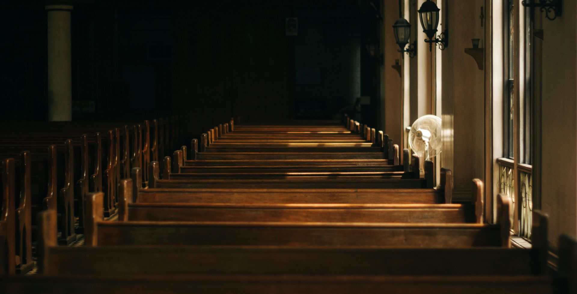 Serene church interior featuring wooden pews and beautiful lighting casting shadows through windows.